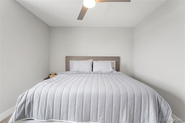 Bedroom with a white quilted bed, gray headboard, and ceiling fan.