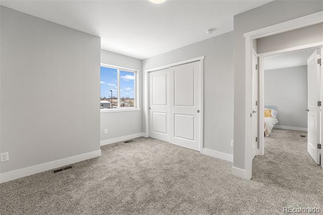 Empty carpeted bedroom with white double closet doors and a window overlooking the neighborhood.