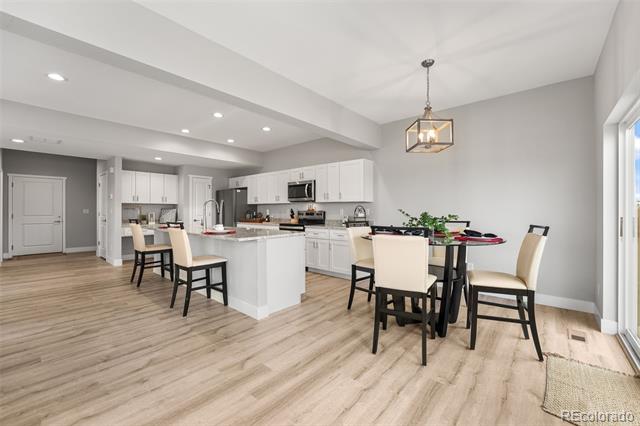 Open-plan kitchen and dining area with a white island and dining table beside tall windows.