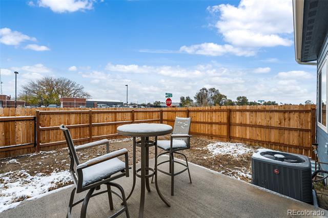 Concrete patio with a round table and chairs, fenced snowy yard, and outdoor HVAC unit.