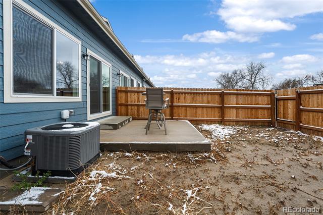 Backyard patio beside a blue-sided home, enclosed by a wooden fence with patches of snow.
