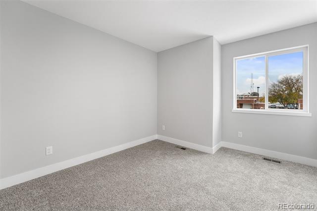 Unfurnished bedroom with gray carpet and a window overlooking a tree and nearby buildings.