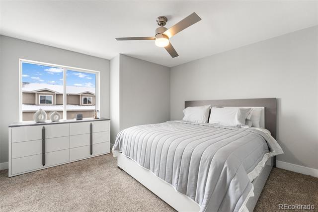 Bedroom with white bedding, a ceiling fan, and a window overlooking neighboring homes.