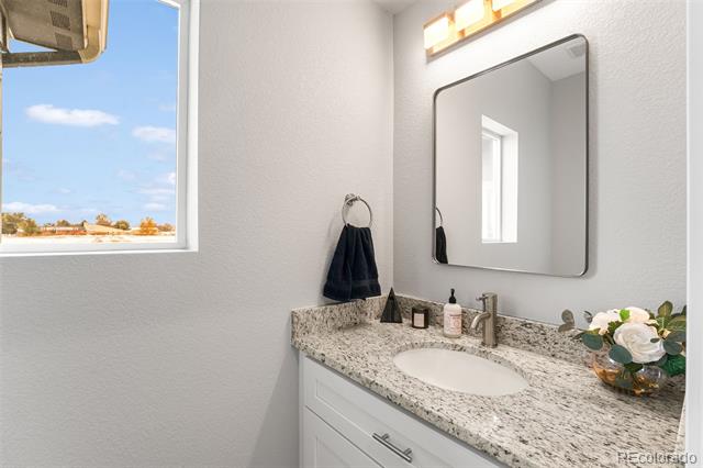Bathroom vanity with speckled granite countertop, rectangular mirror, and a window overlooking open land.