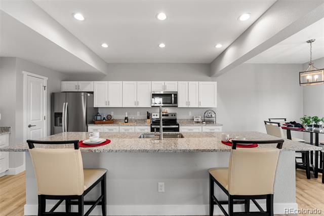 Open kitchen with white cabinets, stainless steel appliances, and a granite island with two bar stools.