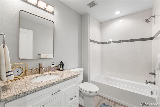 Bathroom with a stone-topped white vanity, wall mirror, and bathtub-shower with dark tile accent.