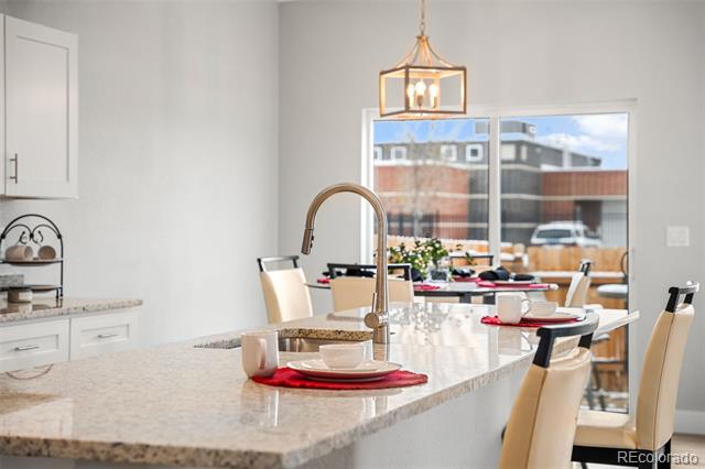 Bright kitchen with a stone island, gooseneck faucet, pendant light, and dining area by large windows.