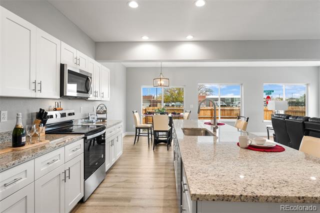 Open-plan kitchen with white cabinets, stainless appliances, and a large granite island overlooking the dining area.