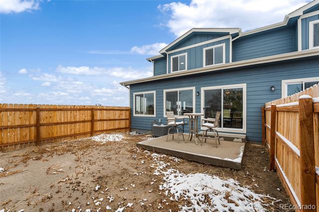 Blue-sided home with a fenced patio and patches of snow in the yard.