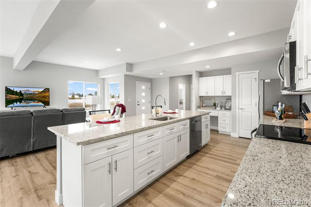 Open-plan kitchen with a large white island, stone countertops, and an adjoining living area.