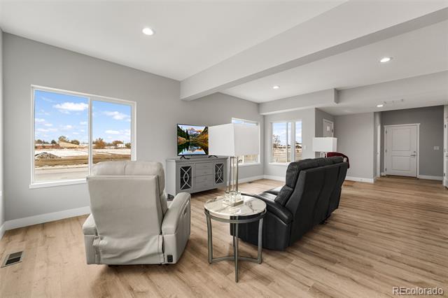 Living room with large windows, a white recliner, black sofa, and light wood floors.