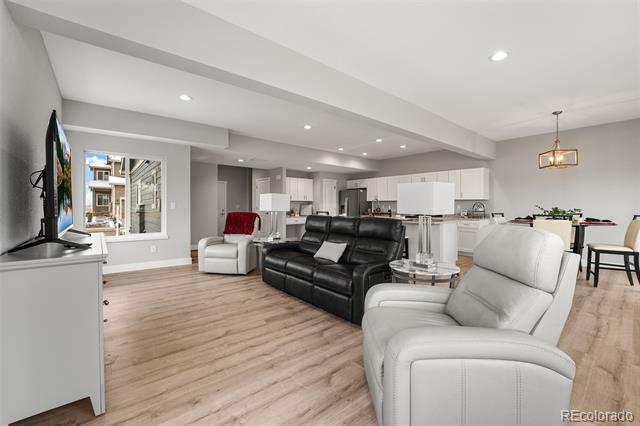 Open-plan living room with black and white leather recliners beside a kitchen and dining area.
