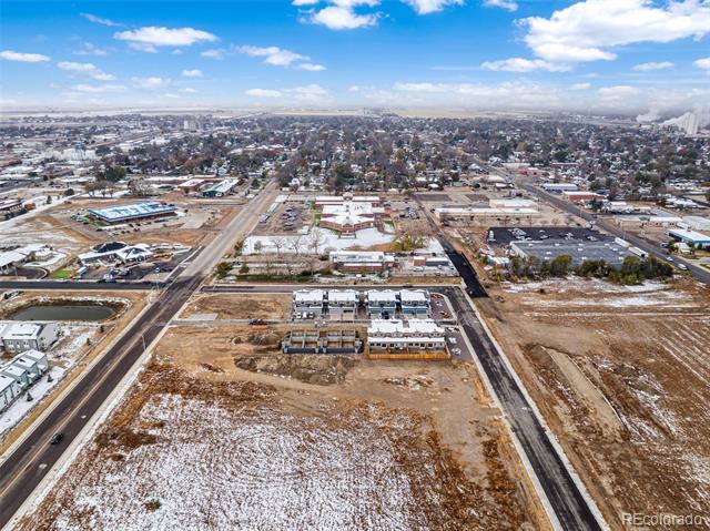 Aerial view of partially built structures and a snow-dusted development area among roads and town buildings.