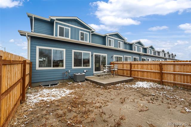 Blue-sided home with a fenced patio, outdoor chairs, and patches of snow.