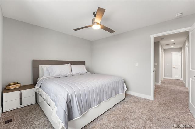 Staged bedroom with white bedding, a gray headboard, and an open doorway to the hallway.