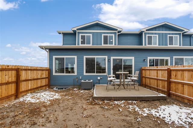 Blue two-story home's fenced backyard with a raised patio and patches of snow.