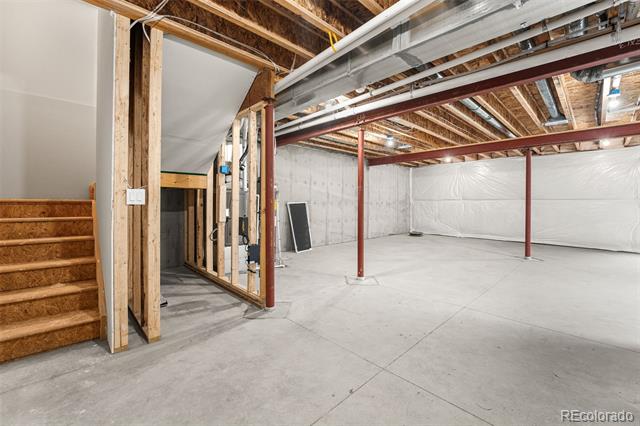 Unfinished basement with a concrete floor, exposed framing, steel support posts, and a wooden staircase.