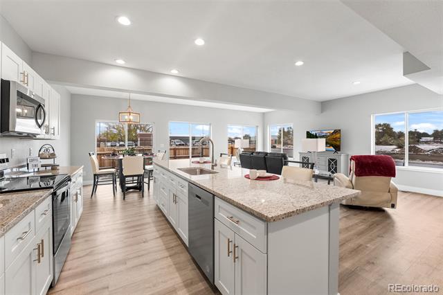 Open-plan kitchen and living area with a large granite island, white cabinets, and wide windows.