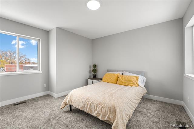 Staged bedroom with a cream-covered bed, mustard-yellow pillows, and a large window.