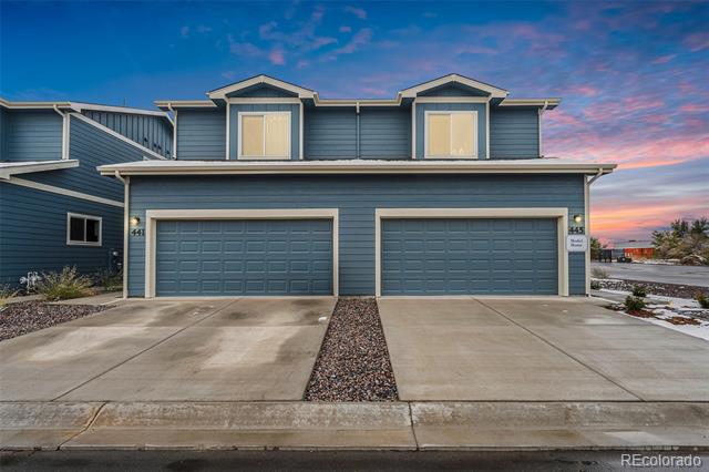 Blue two-unit residence with paired garages and broad concrete driveways at sunset.