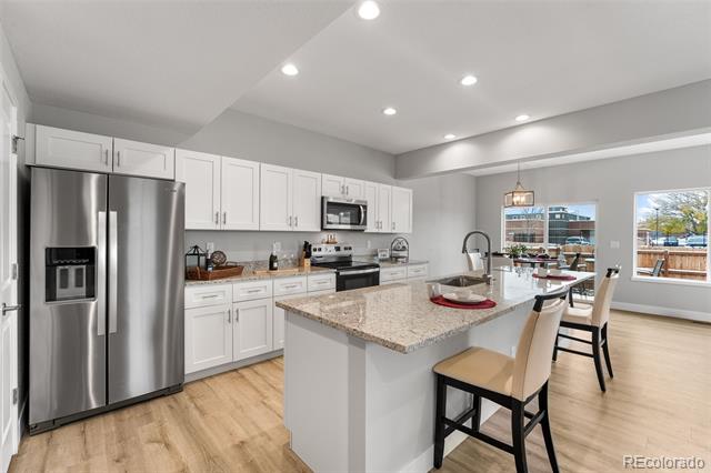 Kitchen with white cabinets, stainless steel appliances, and a large granite island with seating.
