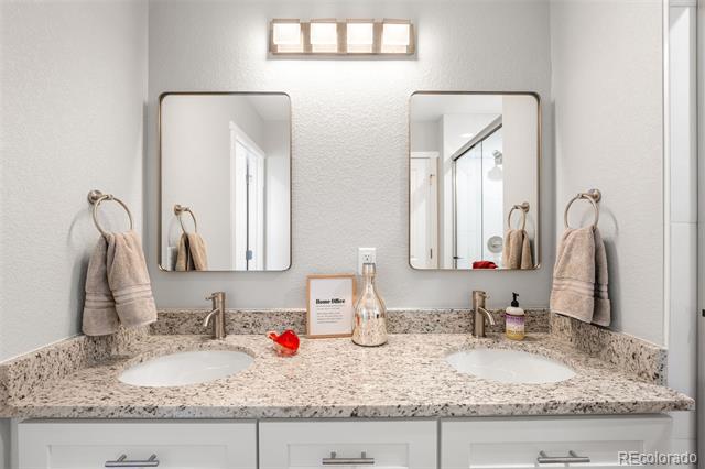 Bathroom vanity with two sinks, a speckled countertop, paired mirrors, and towels on wall-mounted rings.
