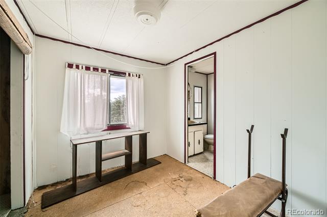 Bedroom with a curtained window, narrow table, worn flooring, and an open doorway to the bathroom.