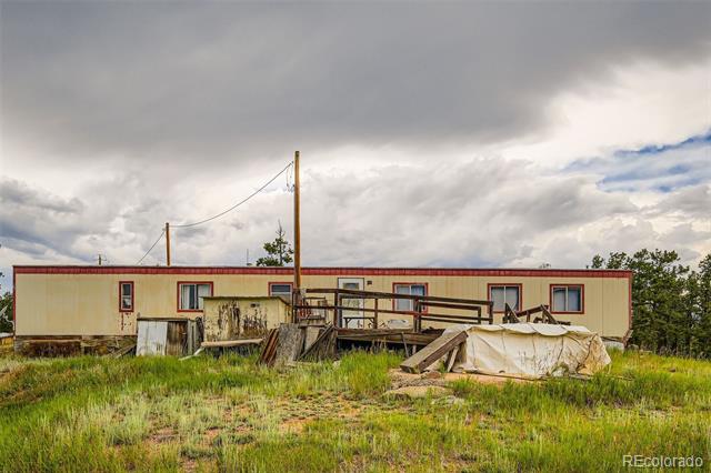 Long beige home with red trim, a rough wooden platform, construction materials, and a tarp in front.