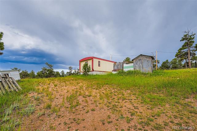 Rural property with a small cream building, red trim, and weathered outbuildings.