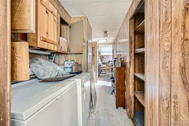 Laundry room with white washer and dryer, wood cabinets, and open shelves along a narrow passage.