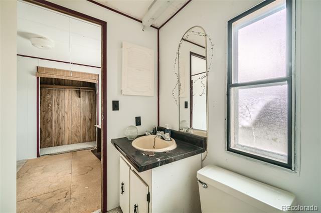 Bathroom with a dark stone vanity, oval mirror, and large window beside a wood-paneled doorway.