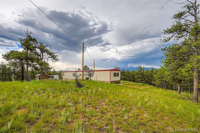 Small red-trimmed outbuilding on a grassy, tree-lined lot with distant mountains.