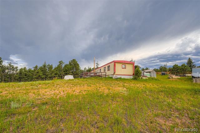 Beige home with red trim and an attached deck on a grassy, tree-lined lot.