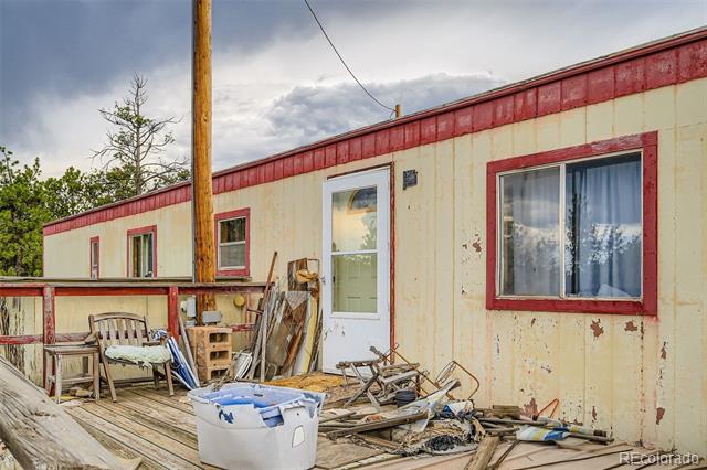 Weathered home with red trim, a white entry door, and a cluttered wooden deck.