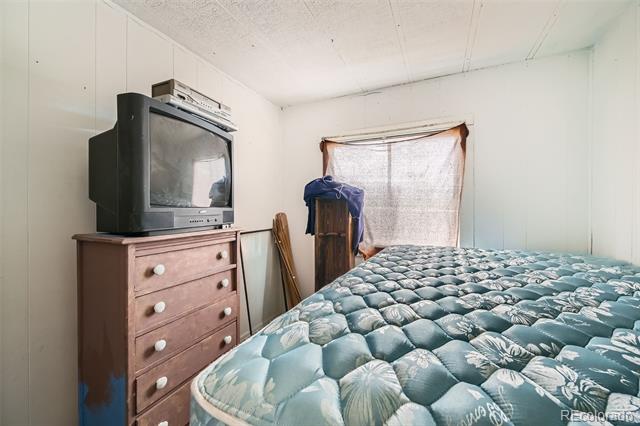 Bedroom with a patterned mattress, wooden dresser, older television, and shaded window.