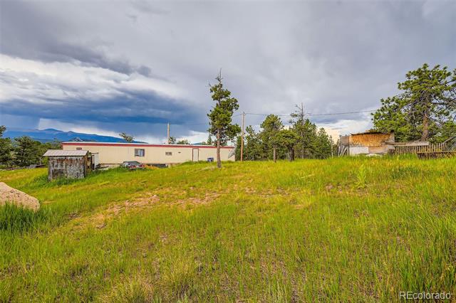 Grassy property with a low building, scattered trees, and distant mountains beneath cloudy skies.