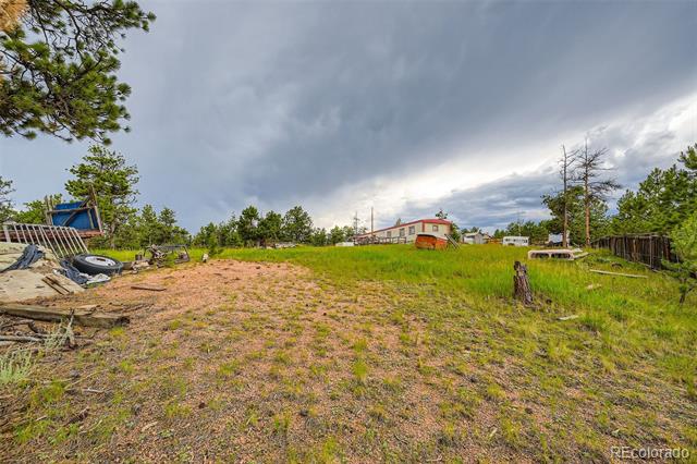 Rural property with a grassy lot, scattered materials, and a small red-roofed building.