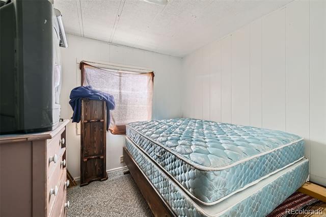 Bedroom with a turquoise quilted mattress, a shaded window, and a television on a dresser.