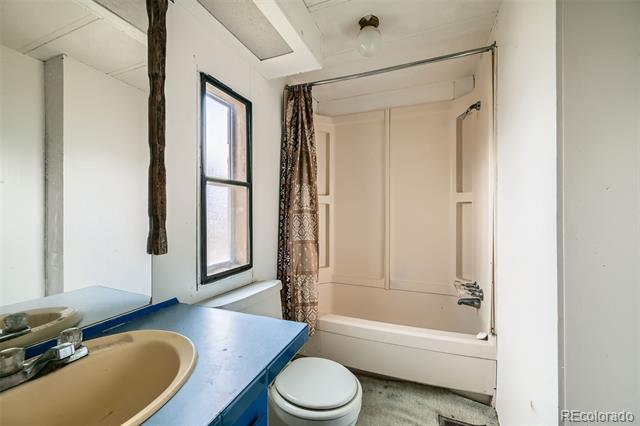 Bathroom with blue vanity, beige sink, toilet, and built-in tub beside a narrow window.