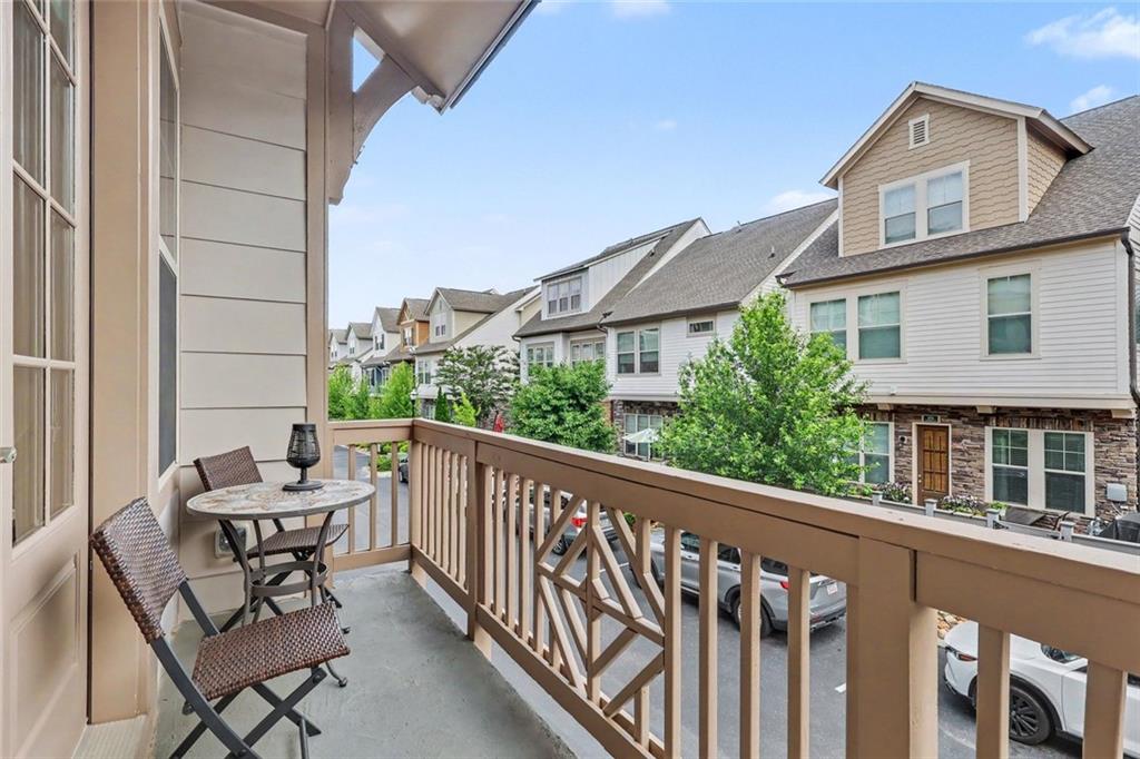 Covered balcony with woven chairs and a small table overlooking neighboring townhouses.