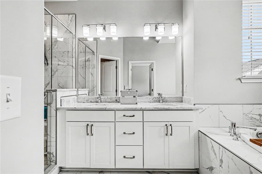 Bright bathroom with a marble-topped vanity, glass shower, and bathtub.