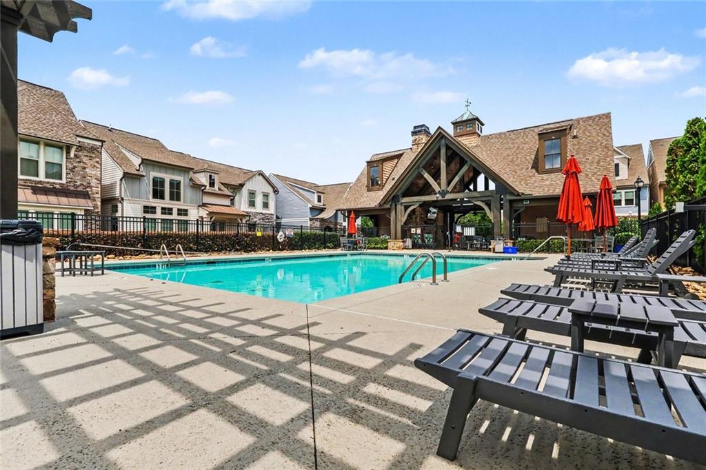 Community pool with black lounge chairs and red umbrellas beside a timber-framed clubhouse.
