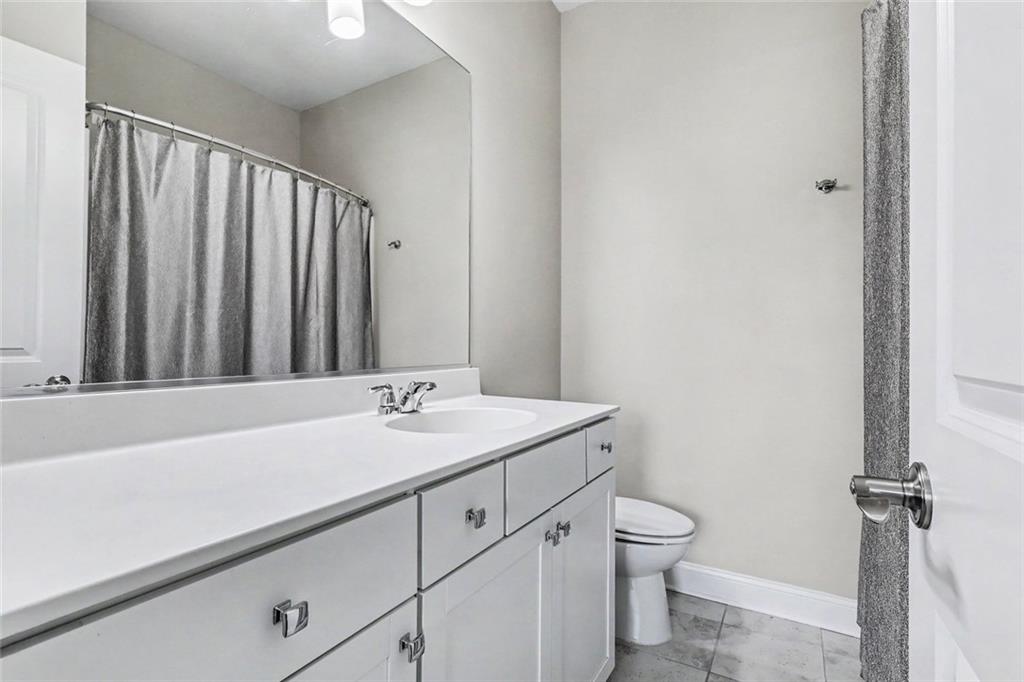 Bathroom with a long white vanity, large mirror, gray shower curtain, and tiled floor.