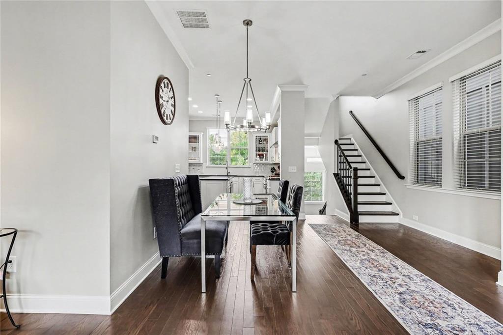 Dining room with a glass-top table, upholstered seating, dark wood floors, and an open staircase.
