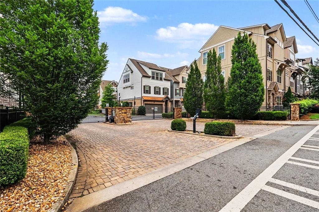Townhome community entrance with a gate, brick paving, and landscaped grounds.