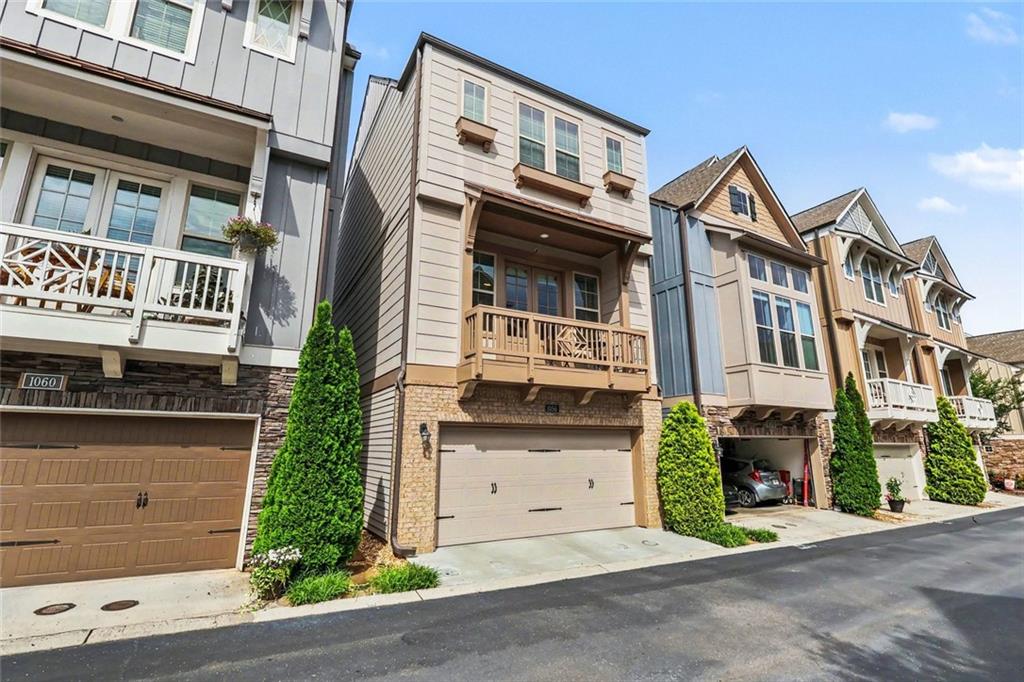 Attached townhomes with balconies, stone accents, and garages along a residential street.