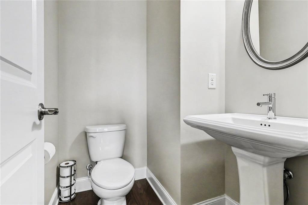 Powder room with a white pedestal sink, toilet, oval mirror, and dark wood flooring.