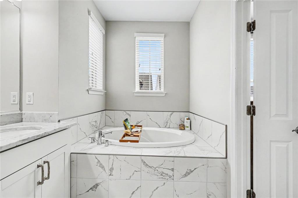 Bathroom with a corner soaking tub, marble-look tile, and two windows with blinds.