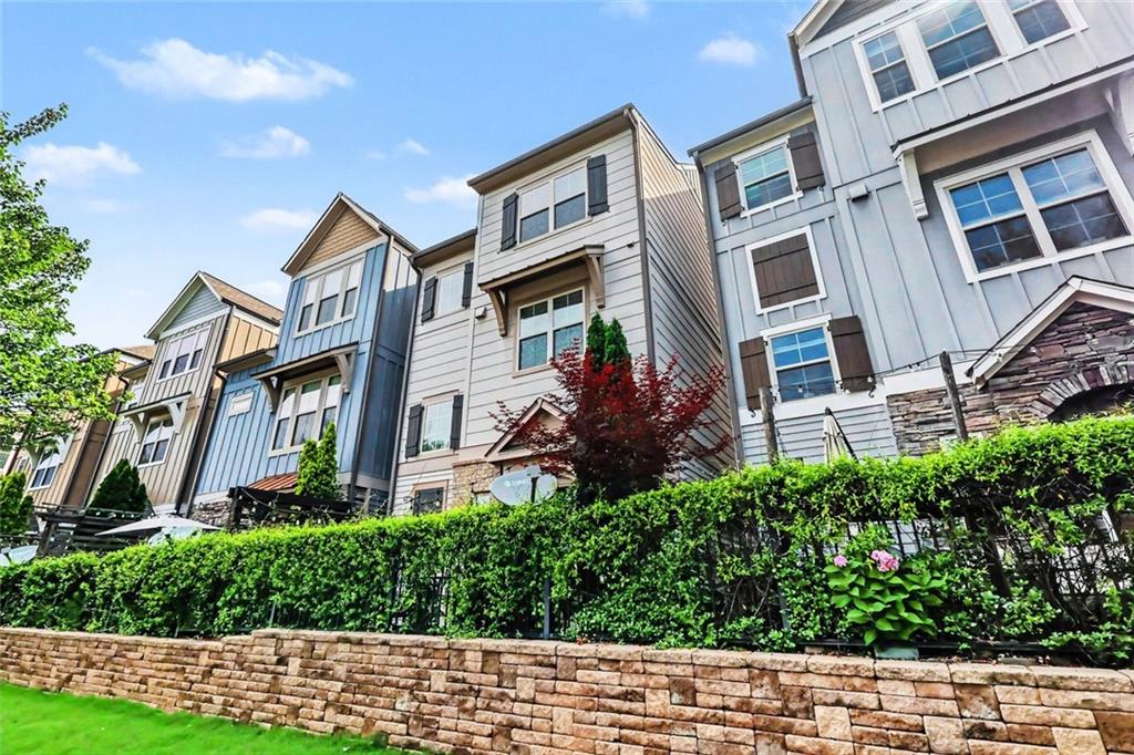 Row of attached homes with varied siding, stone accents, and a hedge above a stone retaining wall.