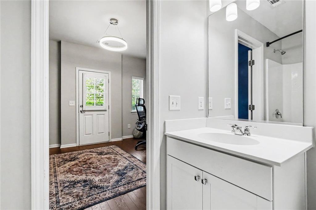 Bathroom vanity and mirror overlooking a room with a patterned rug and desk chair.